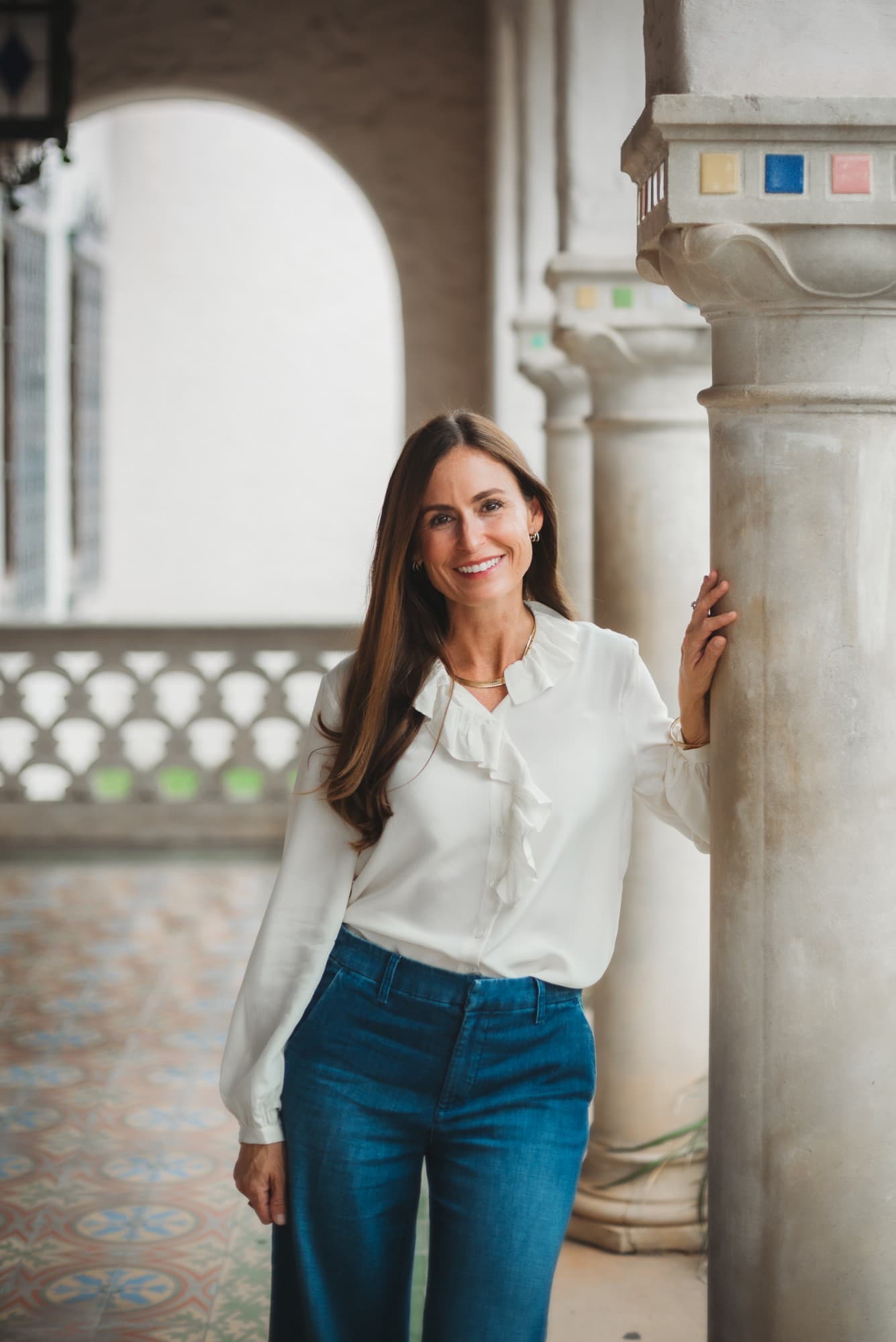 Dominique Balldin smiling beside a stone column under a row of arches
